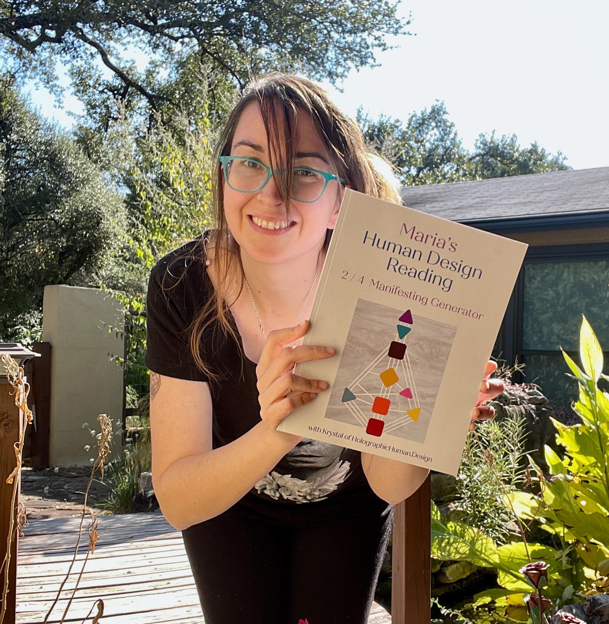 Krystal Linnea - Image of Krystal Linnea standing outside in a garden, holding up a full-colour 96-page printed Human Design Chart book